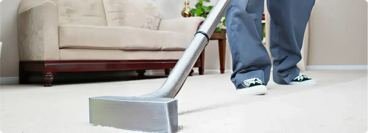 Carpet cleaning technician using a hot-water extraction wand on a light-colored carpet in a living room, Grand Rapids, MI.