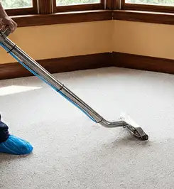 Steam carpet cleaning technician using a hot-water extraction wand on a residential carpet, wearing blue protective shoe covers Grand Rapids, MI.