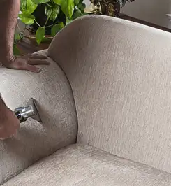 Professional upholstery cleaner deep-cleaning a fabric sofa with a handheld extraction tool and hose Grand Rapids, MI.