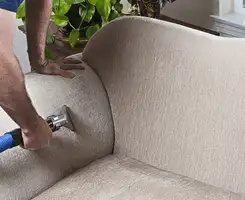 Professional upholstery cleaner deep-cleaning a fabric sofa with a handheld extraction tool and hose in Grand Rapids, MI.